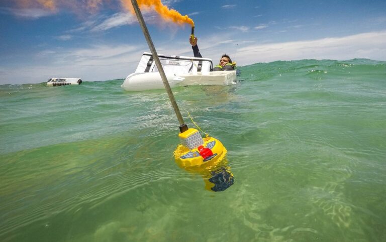 Ocean Signal EPIRB1 floating in ocean while person signals for rescue